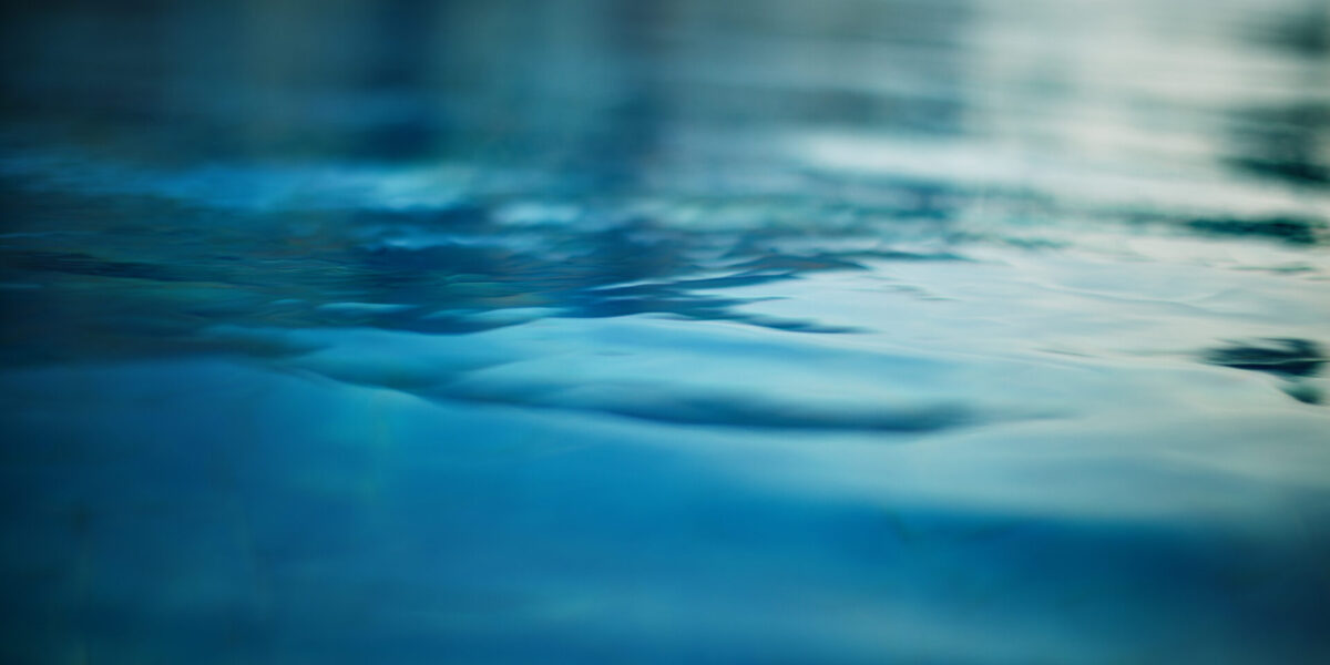 A close-up view of calm, rippling blue water, softly blurred, reflecting light and creating a tranquil, serene atmosphere.