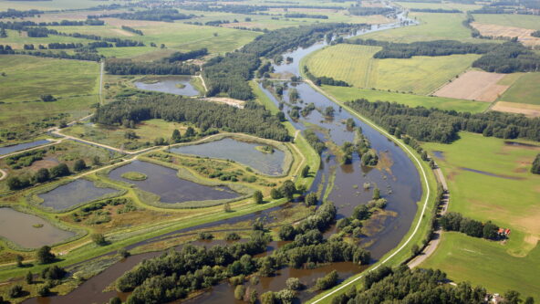 Aerial view of a river winding through a rural landscape, with green fields, wooded areas, and patches of wetlands—ideal for Messdatenmanagement to monitor environmental changes along roads and tree-bordered waterways.