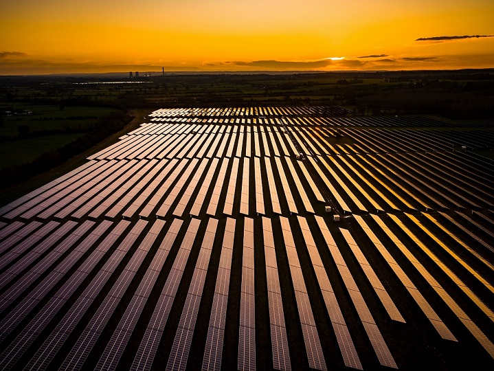 A large solar farm with rows of solar panels reflecting the golden sunset, set in a rural landscape. Real-time hail sensors help protect the panels, ensuring reliability amid fields and distant trees under a colorful sky.