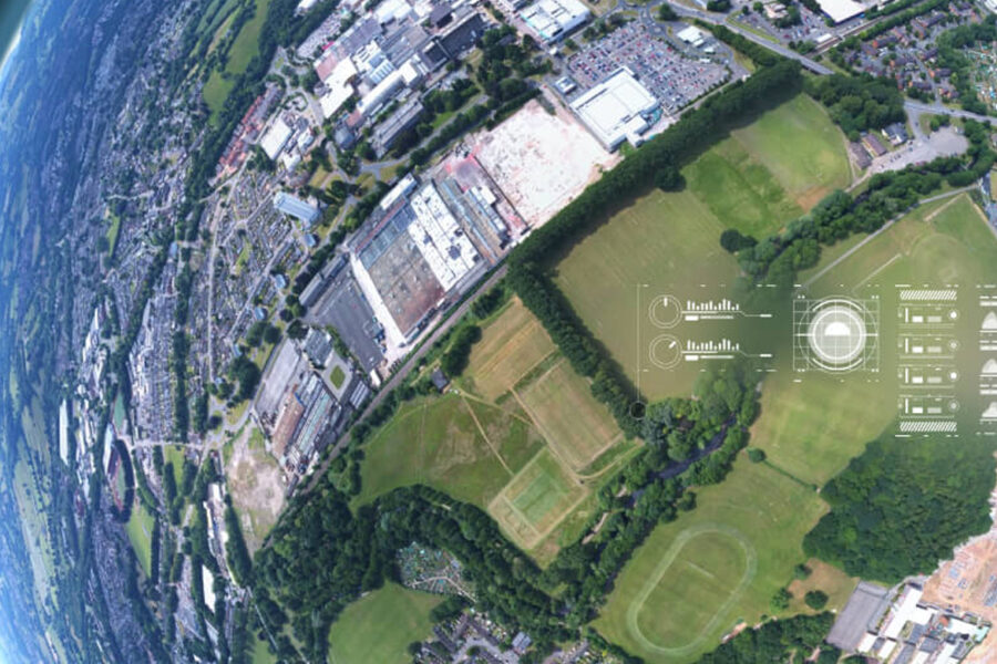 Aerial, wide-angle view of a city bordered by green fields and trees, with digital graphs and real-time hail sensor data overlays appearing on the landscape, suggesting analysis or monitoring. The Earth’s curve is visible on the left.
