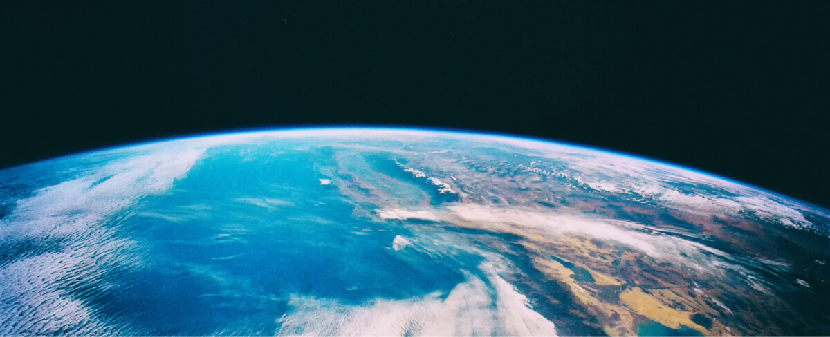 View of Earths curved horizon from space, showing blue oceans, white clouds, and brown landmasses under a dark, black sky.