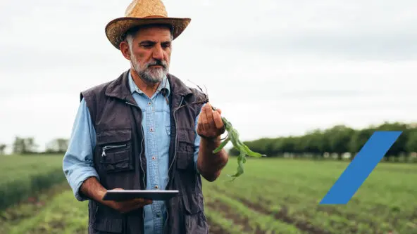 A farmer wearing a hat and vest examines a plant while holding a tablet in a large green field, highlighting Data-Driven Water Management. Trees and a cloudy sky form the background, with a blue diagonal stripe overlaid on the image.